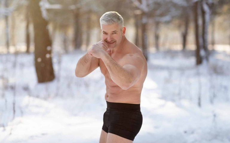 Handsome senior man with bare chest standing in fighter pose in winter forest. Acclimation concept