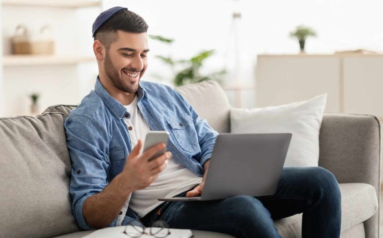 Happy jewish man using mobile phone and laptop